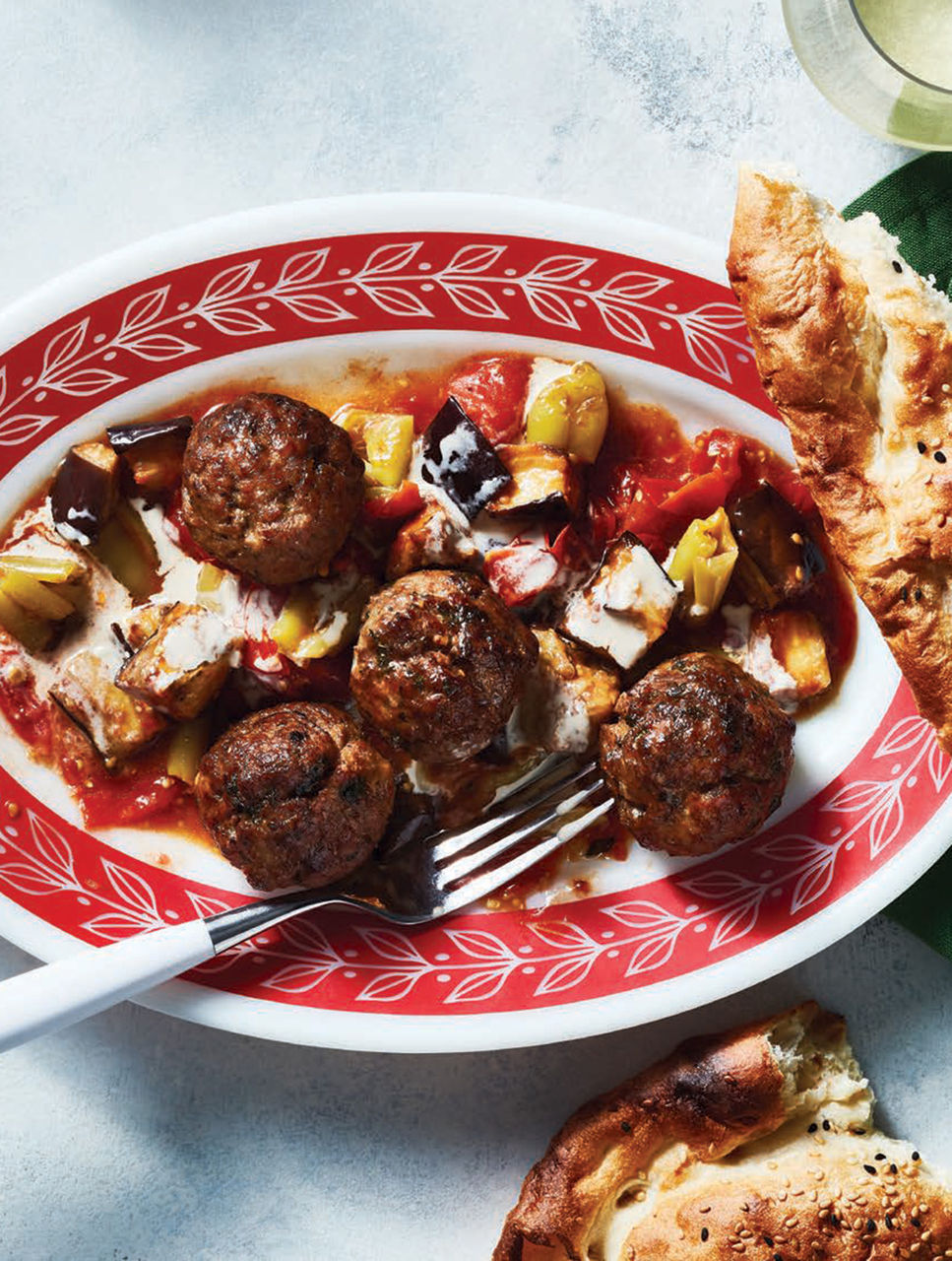 Boulettes de viande et aubergines rôties sur plaque, arrosées de sauce au tahini