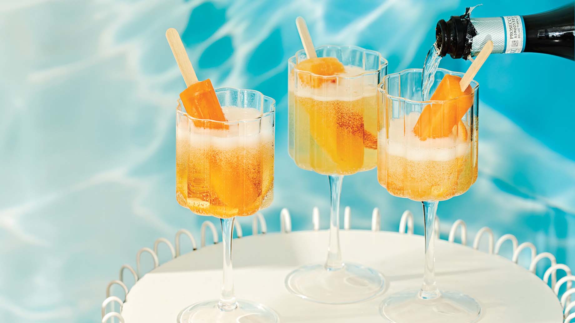 Peach and orange ice pops dipped in glasses sparkling wine